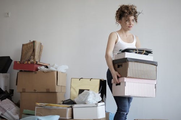 A woman carries unorganized, messy boxes and belongings for storage.