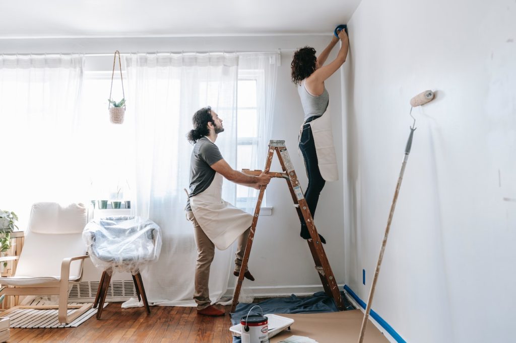 A woman scrubbing a wall while the husband holds the ladder, she is on